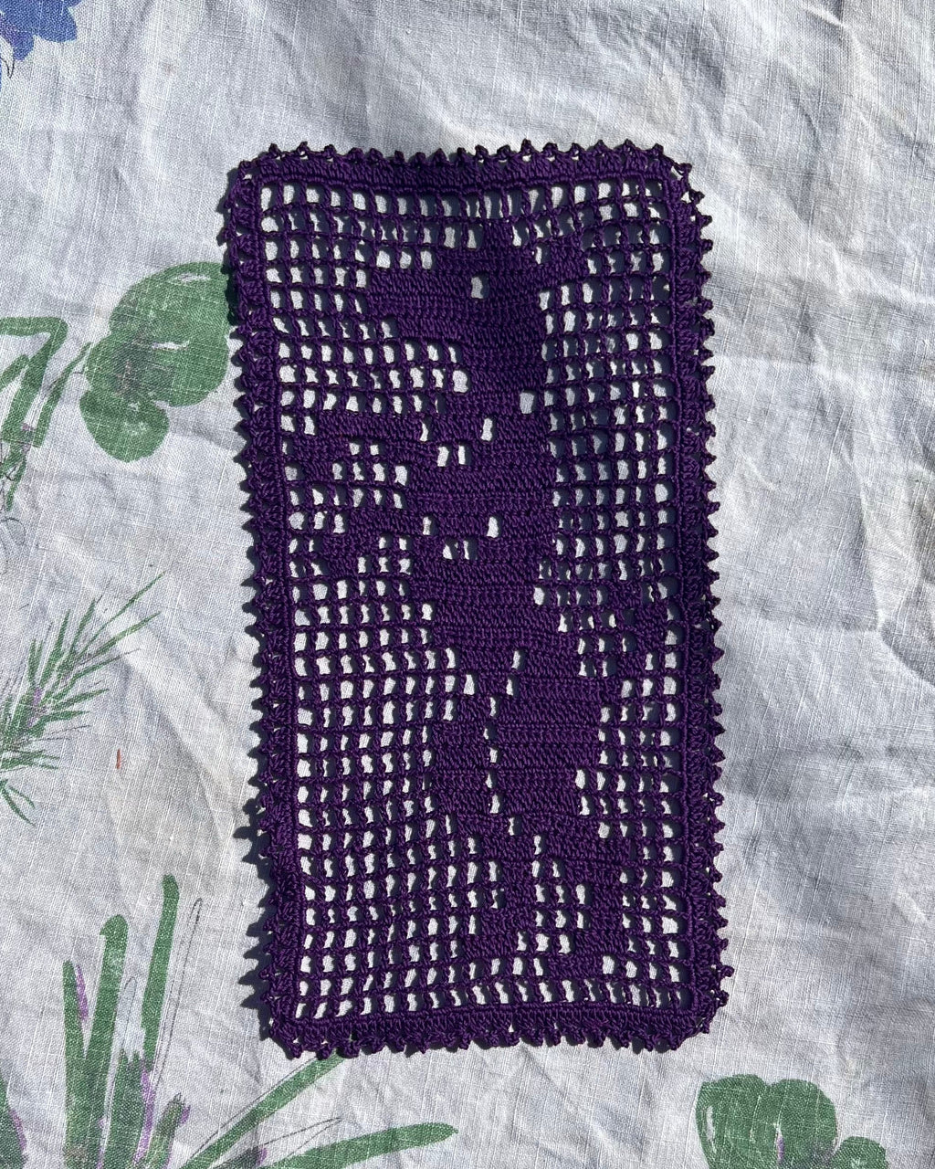 A purple filet crochet doily with the image of a dog standing and begging.